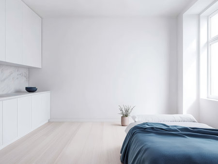 A minimalistic bedroom featuring a low bed with a blue blanket, a small plant in a pot, and bright sunlight illuminating the space from large windows.の素材