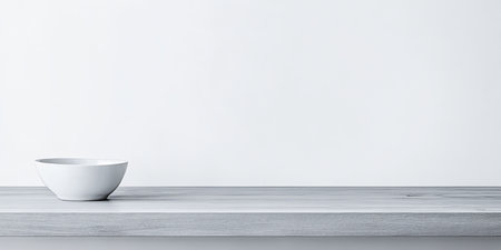 A white ceramic bowl rests on a light wooden shelf, showcasing a minimalistic design. The background is bright and simple, enhancing the bowl's elegant appearance.の素材