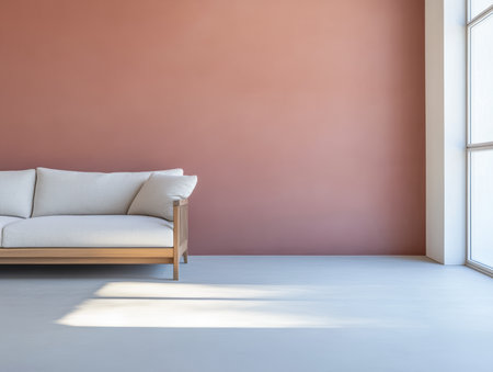 A light-colored couch sits against a warm-toned wall in a spacious living room. Sunlight streams through large windows, creating a calm and inviting atmosphere.の素材