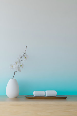 A white vase holds delicate flowers on a wooden table. Two smooth white objects rest beside it. The background features a gentle gradient of soft color, creating a calm atmosphere.の素材