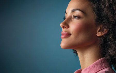 A young woman with curly hair and natural makeup smiles softly while looking to the side. She is dressed casually and appears thoughtful in a calm atmosphere.の素材