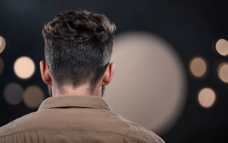 A man faces away from the camera, showcasing his modern hairstyle. Soft bokeh lights form a dreamy backdrop, enhancing the mood of the evening gathering.の素材