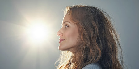A woman with long, flowing hair sits peacefully, her profile highlighted by a gentle glow. She reflects tranquility and poise in a calm indoor environment.の素材