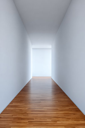 A spacious corridor features clean white walls and polished wooden flooring, leading to a bright light at the far end. The minimalist design conveys calmness and openness.の素材