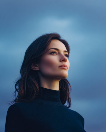 A woman stands outdoors, gazing up at the cloudy sky. The dusky light frames her face, creating a calm and contemplative atmosphere. Her expression shows deep thought and connection with nature.の素材