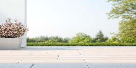 A serene terrace features a white planter with vibrant flowers. Lush green grass and trees are visible in the distance, under clear blue skies.の素材