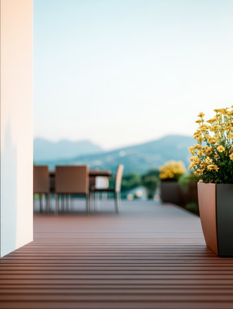 A spacious wooden deck features a dining table with chairs, surrounded by vibrant flower pots. Distant mountains are visible under a clear sky, creating a serene atmosphere.の素材