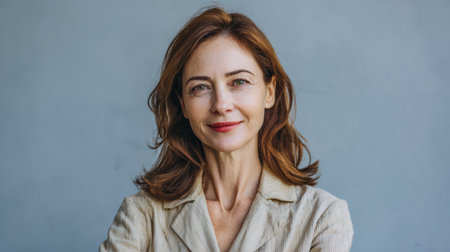 A woman stands confidently with her arms crossed in front of a plain background. She smiles while wearing a light-colored suit. The scene is bright and clear.の素材