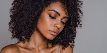 A woman stands in a bright space, her curly hair falls gently around her shoulders. She has her eyes closed, showing a calm expression on her face. The light creates soft shadows.の素材