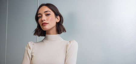 A young woman stands confidently with her arms crossed in front of a textured wall. She wears a light outfit and appears focused, adding to the modern indoor atmosphere.の素材