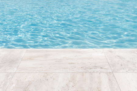 Clear water in a swimming pool shows bright reflections under the sun. The surface appears smooth and inviting, surrounded by light-colored tiles.の素材