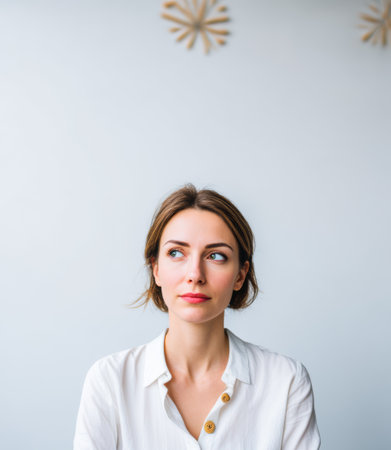 A woman with light hair sits in a room with plain walls. She looks thoughtfully to the side, reflecting on something important while the decor is minimal.の素材