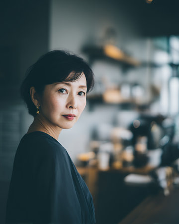A woman stands in a cafe, gazing thoughtfully. She is dressed simply and surrounded by shelves filled with items. Soft lighting creates an inviting atmosphere in the room.の素材