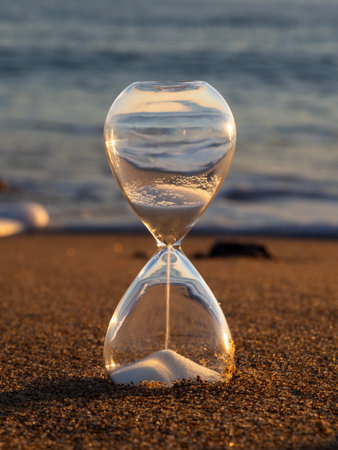 Hourglass on the beach at sunset time. Concept of time passing.の写真素材