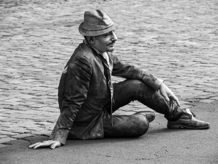 Handsome man in hat and leather jacket sitting on the pavementの写真素材