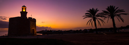 Silhouette of a lighthouse and palm trees at sunset on the Mediterranean coast
