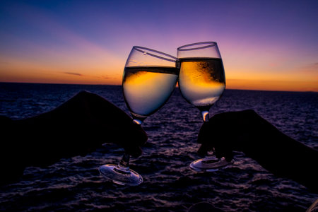 Silhouette of a couple clinking glasses with white wine at sunset