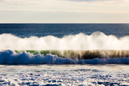 A powerful Southern Ocean wave crashes into shore, as the spray is illuminated in soft evening light...
