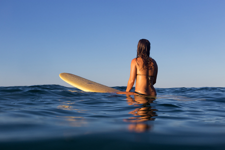 A beautiful surfer girl sits on her board and waits for a wave on a glassy calm ocean in Australia.の写真素材