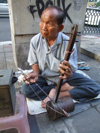 BANGKOK, THAILAND - APRIL 03: Elderly Thai blind man sits by the roadside and plays music for passing tourists and Thai people to make money. April 03 2007 in Bangkok. のeditorial素材