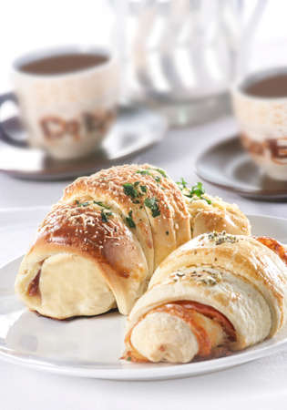 Two croissants on a plate with coffee cups out of focus in the background