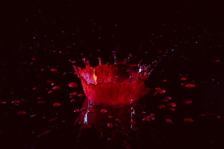 Stop action photo of water drop spashing on red liquid creating a crown effect.の写真素材