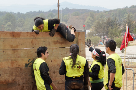 Team of young latin athletes helping each other to climb a wooden wall obstacle in a Spartan Race...