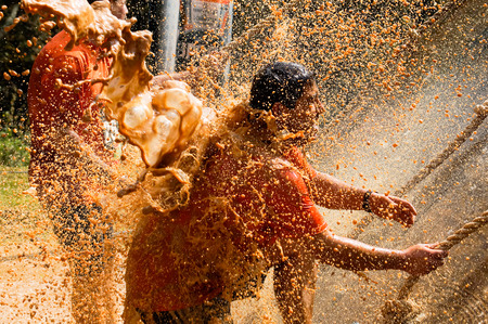 Male crossfit athlete climbing using a rope under a mud shower.のeditorial素材