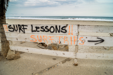 Rustic wood sign offering surf lessons on La Bocana Beach at Huatulco Mexico. Ocean on the background with a cloudy skyの写真素材