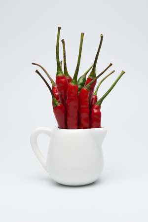 Red fresh chili peppers in the small white jug on white background.の写真素材