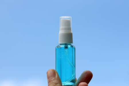 Hand holding Alcohol based hand sanitizer spray on blue sky background. Concept about new normal,social distancing,business,   and travel guideline for prevention of Covid-19 (Coronavirus).の写真素材