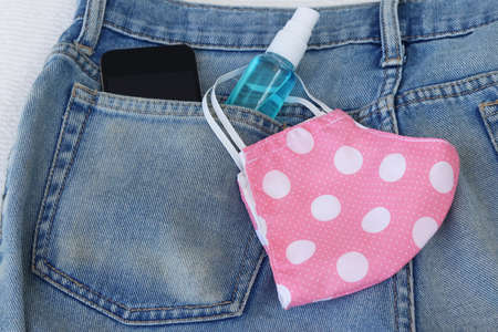 DIY cloth face mask ,hand sanitizer spray and smart phone in jean back pocket background. Concept for the new normal or new lifestyle after COVID-19 Coronavirus pandemic.の写真素材