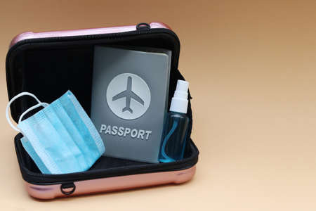 Passport with small suitcase,medical mask and hand sanitizer spray on cream color background with copy space. Lifestyle and traveling concept in New Normal after Covid-19 / Coronavirus pandemic.の写真素材