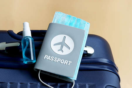 Passport with medical mask and hand sanitizer gel placed on suitcase on cream background with copy...