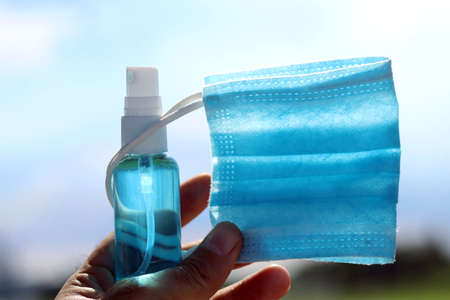 Hand holding medical mask and alcohol based hand sanitizer spray with back light.Concept about new normal,social distancing,business,   and travel guideline for prevention of Covid-19 (Coronavirus).の写真素材