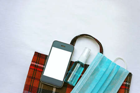 Medical face mask ,hand sanitizer spray and smart phone with mock up placed on cloth bag on white...