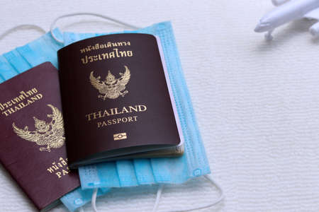 Two Thai Passports with medical face masks and blurred airplane on white background with copy space. Lifestyle and traveling concept in New Normal after Covid-19 / Coronavirus pandemic.の写真素材