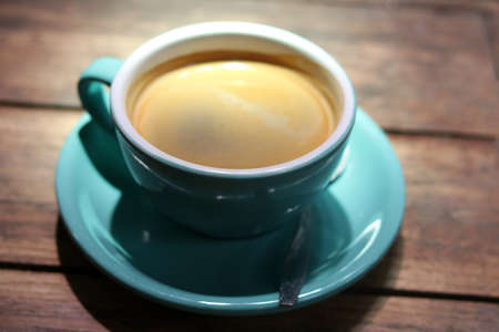Hot black coffee or Americano in blue ceramic cup on wooden table background.