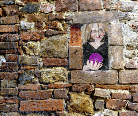 Halloween scary witch holding a glass sphere window peek through a brick wall full of spider websの写真素材
