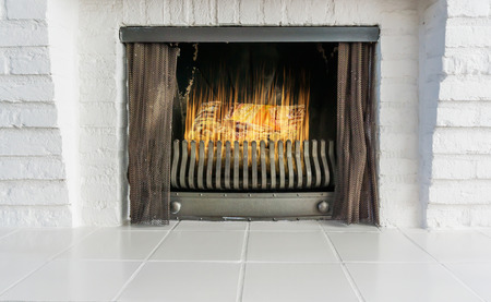 lighted and burning fireplace in retro style but with a modern look background architecture is of white brick stones and white tilingの写真素材
