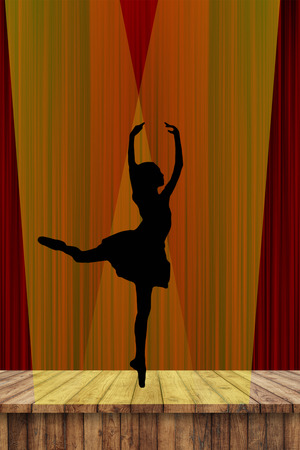 Ballerina silhouette of a young ballet lady dancing on pointe in attitude derriere position on stage in the spotlight with a red curtain backgroundの写真素材