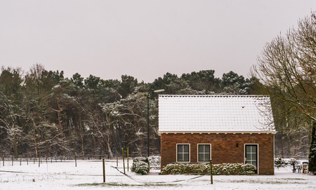 small farmers cottage in a winter landscape scenery, farm fields and house covered in snow, living near the forestの写真素材