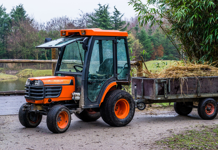 agricultural equipment, orange tractor with a trailer that is filled with hay, farm machineryの写真素材