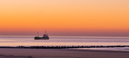 lighted ship sailing in the sea at sunset, the Belgian coast, nature and transport backgroundの写真素材