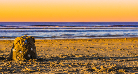 small sandcastle decorated with seashells on the beach at sunset, beautiful blue ocean with a colorful skyの写真素材