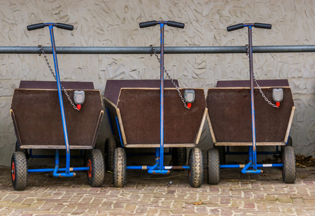 a row of pulling carts for baggage and children, locked and leashed on a metal bar, outdoor...