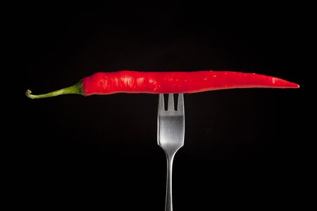 Hot chilli pepper on fork with black backgroundの写真素材