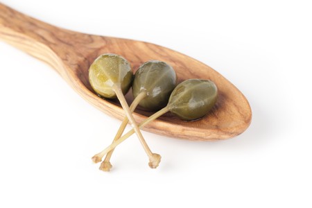 Three large capers in a wooden spoon isolated on a white background.の写真素材