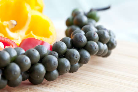 Close up of fresh pepper corns still on the stalk with red and yellow hot peppers in the background.の写真素材