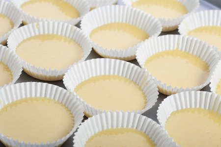 Cupcake papers filled with yellow cupcake batter.
